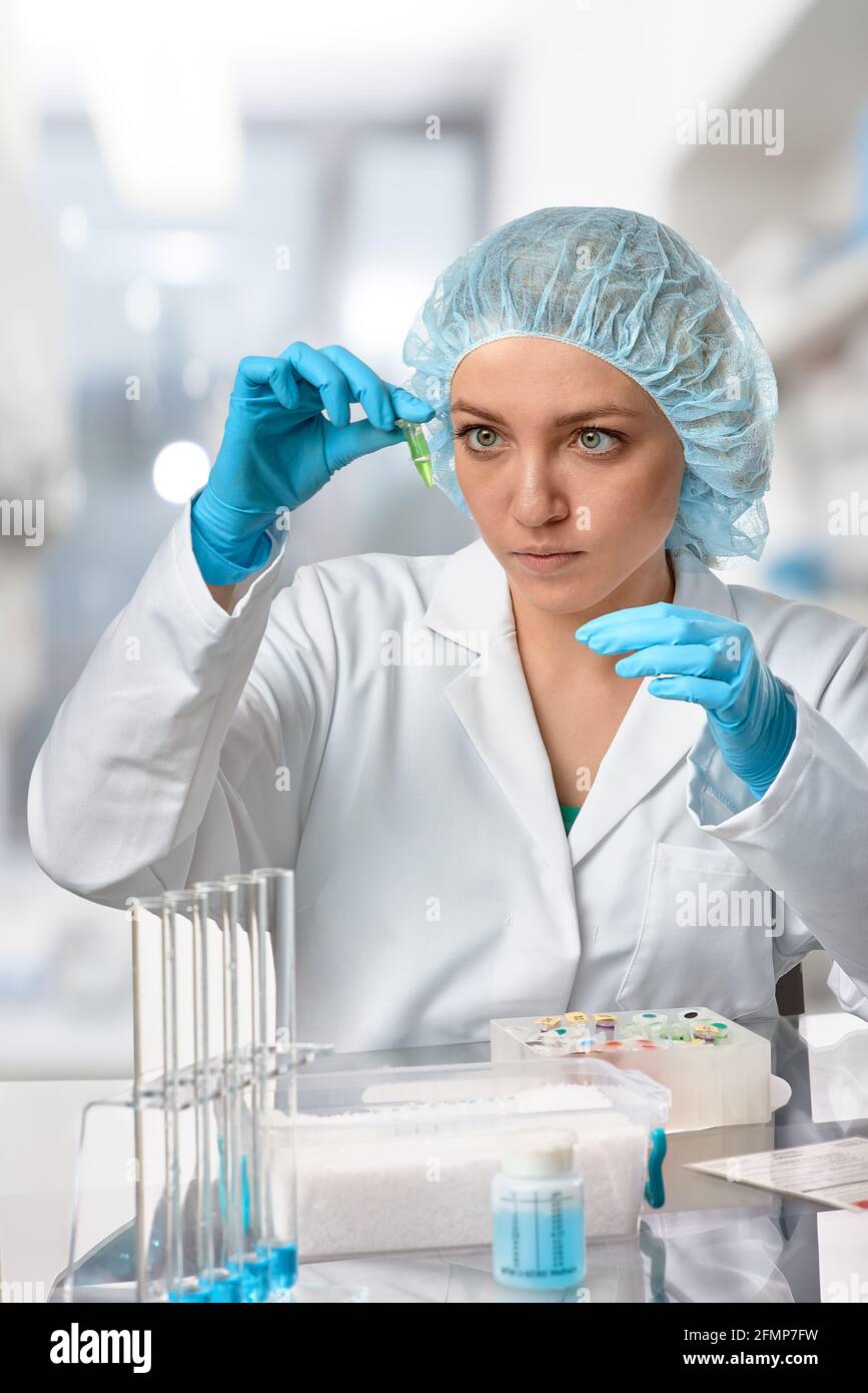 Pharma femme TECH travaille en laboratoire. Jeune femme caucasienne dans  des gants de protection, un chapeau et une blouse blanche échantillon de  pipettes dans un flacon. Intérieur du laboratoire Photo Stock -