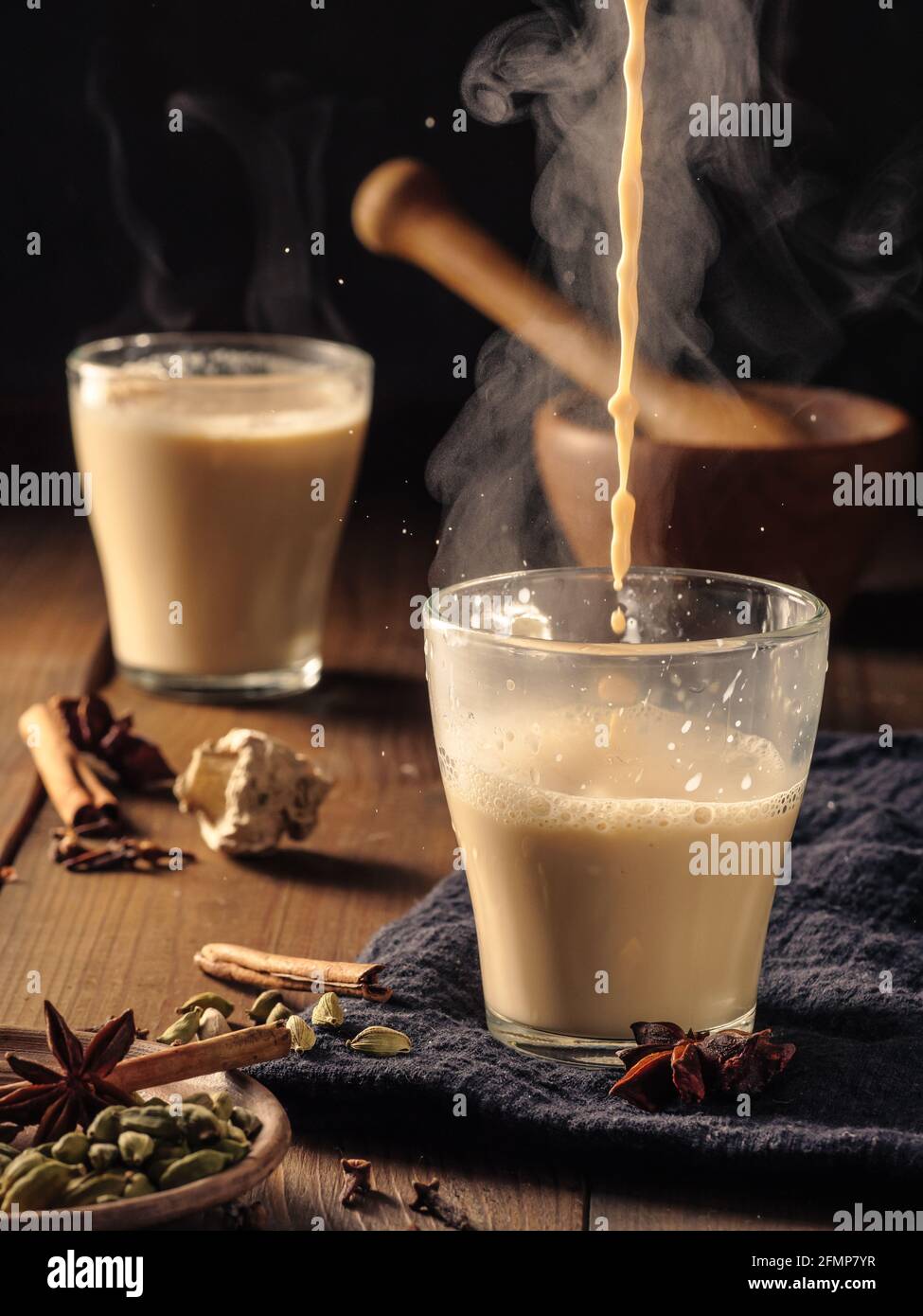 Le thé masala est versé dans une tasse en verre. Les épices sont disposées sur la table. Banque D'Images