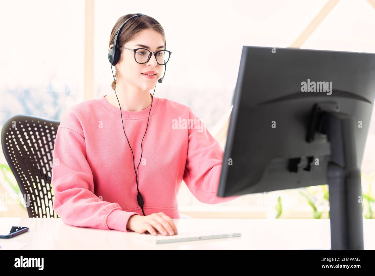 Un assistant du service clientèle portant un micro-casque tout en étant assis derrière son ordinateur et en travaillant à domicile. Bureau à domicile. Banque D'Images