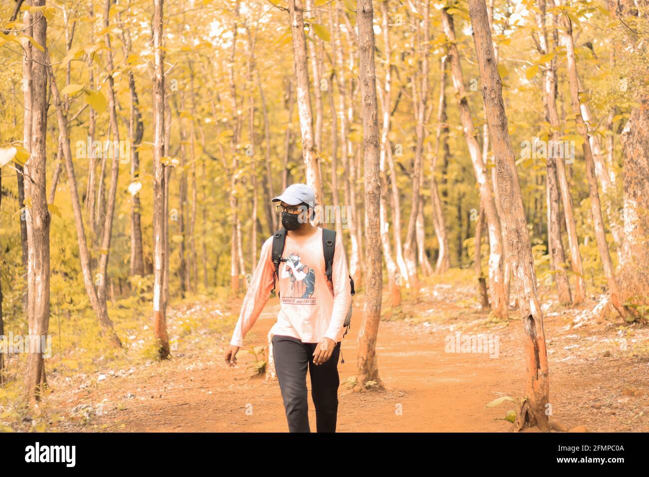 Image cinématographique d'un Indien de 18-25 ans portant un chapeau et un masque et marchant librement dans une jungle au milieu de la pandémie du virus corona. Avec un sac et Banque D'Images