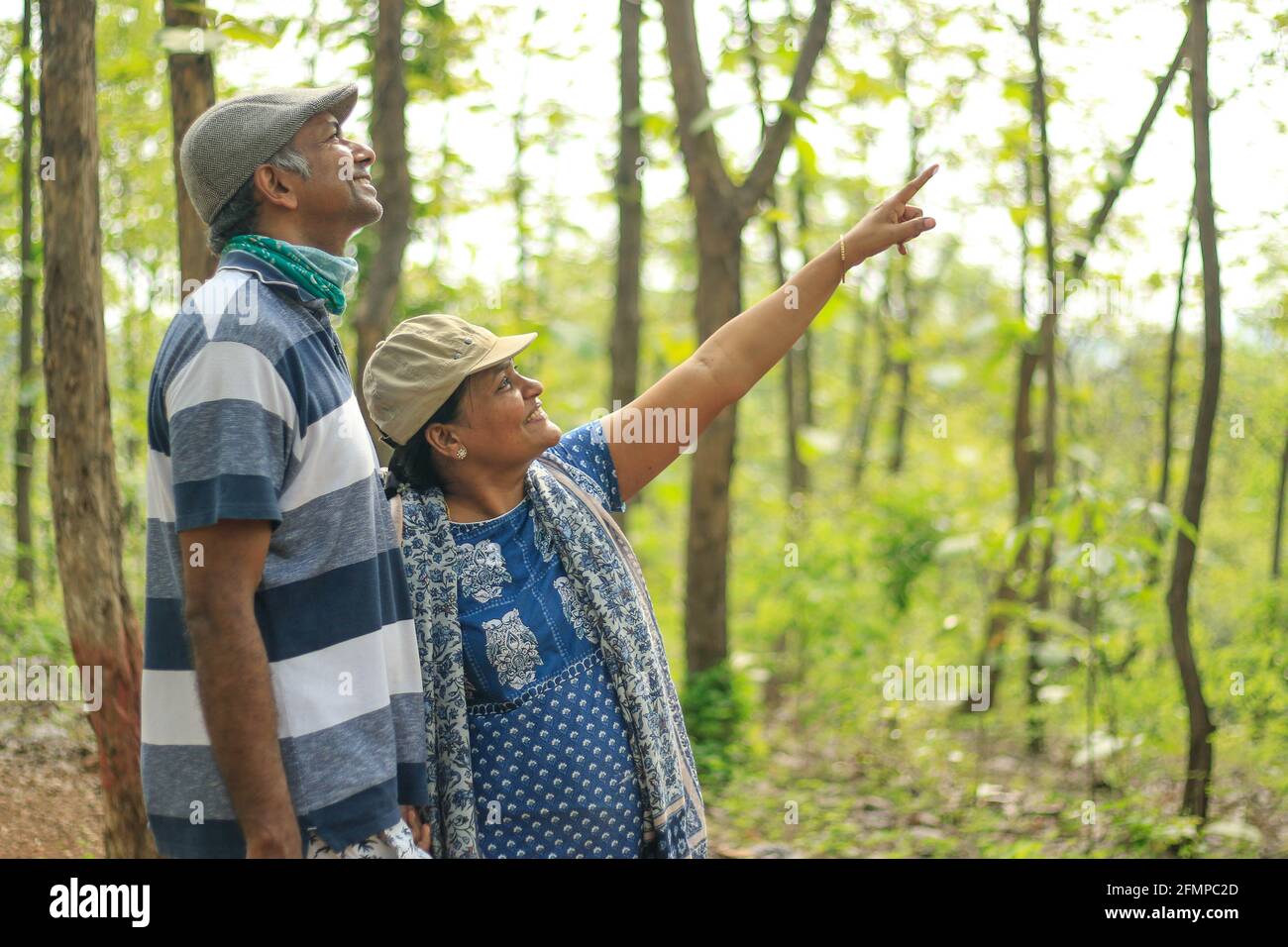 Un portrait d'un couple heureux d'âge moyen marchant dans la forêt et pointant le doigt vers le haut vers quelque chose, avec un arrière-plan vert flou bokeh Banque D'Images