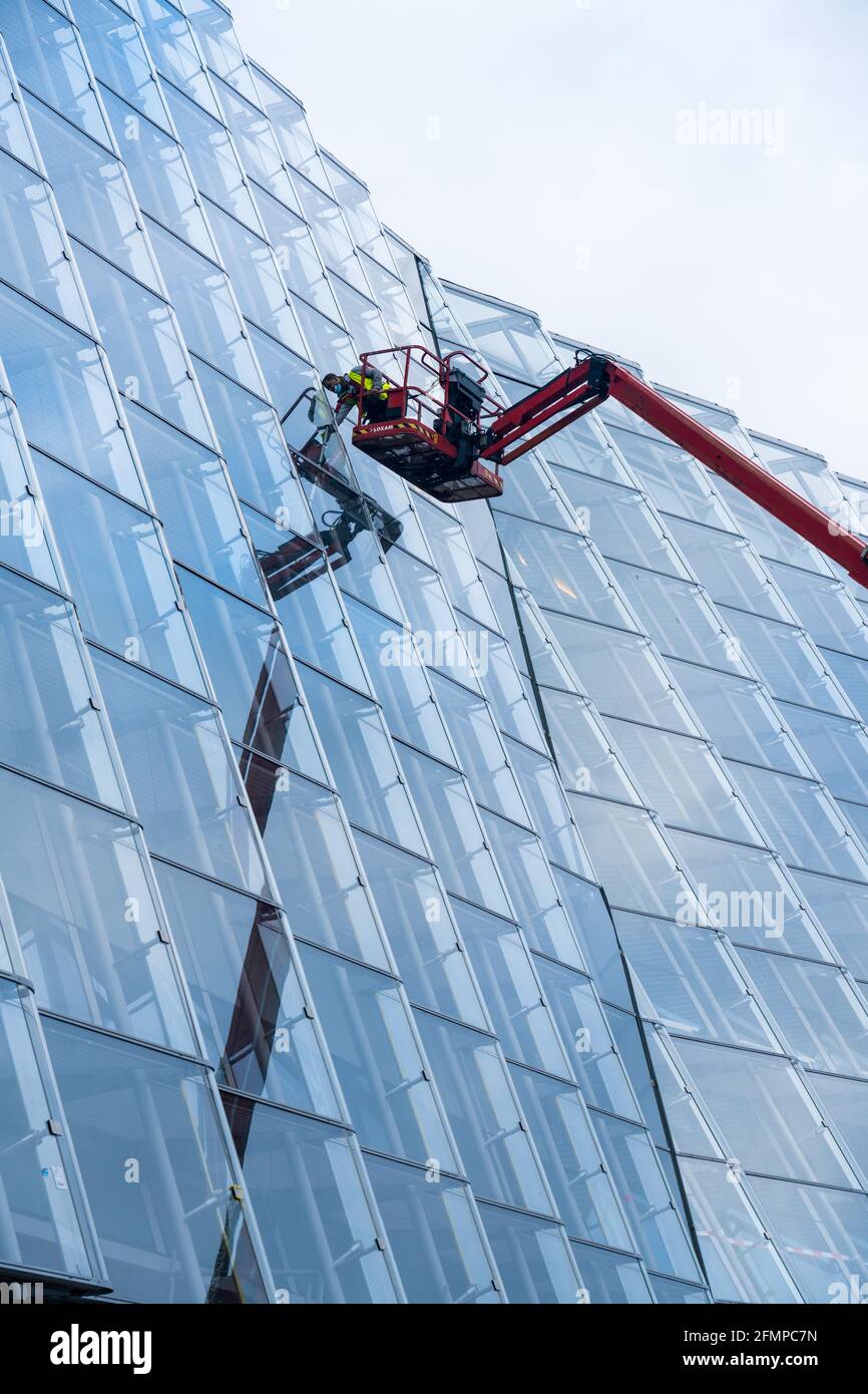 Grue avec ouvrier à la façade de verre avec réflexion Banque D'Images