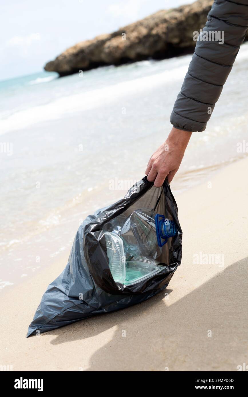 gros plan d'un jeune homme caucasien portant un sac à ordures plein de  déchets fraîchement collectés sur le sable d'une plage solitaire, comme une  action pour nettoyer le Photo Stock - Alamy