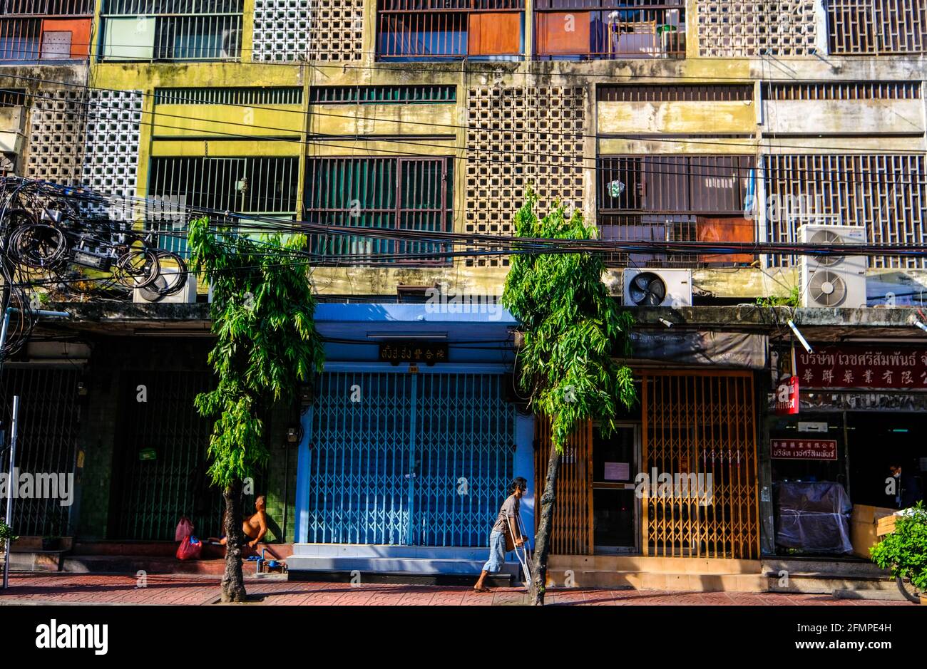 Un homme sur des béquilles passe devant un immeuble multicolore dans le quartier chinois de Bangkok, en Thaïlande. Banque D'Images