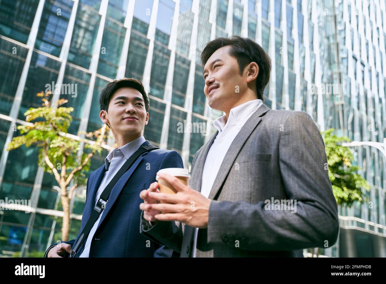 vue latérale de deux employés de bureau asiatiques à col blanc discutant pour les affaires en marchant dans la rue dans le centre-ville moderne Banque D'Images