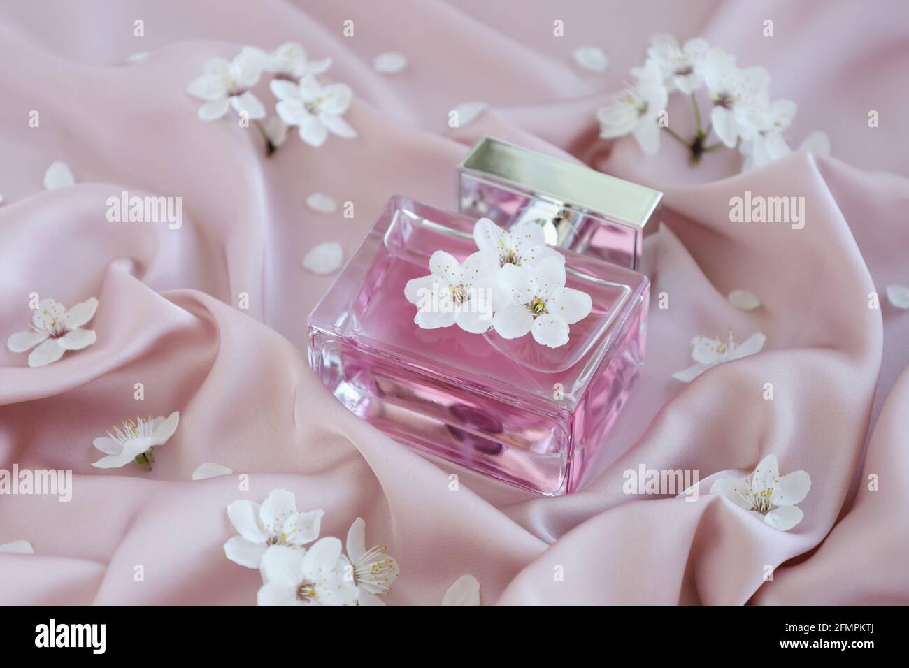 Bouteille en verre de parfum de luxe aromatique sur un tissu en soie rose doux avec fleurs de la branche. Emballage minimaliste, marquage. Floral Banque D'Images