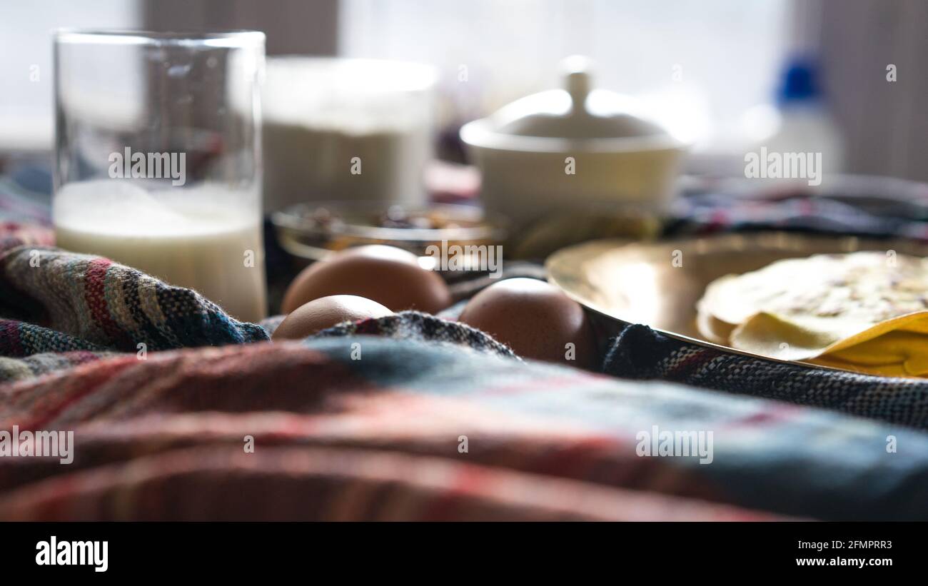 Une pile de crêpes chaudes fraîches sur une table dorée à la maison pour le petit déjeuner, des ingrédients pour faire des crêpes, gros plan des œufs biologiques. Mise au point sélective, à la portée Banque D'Images