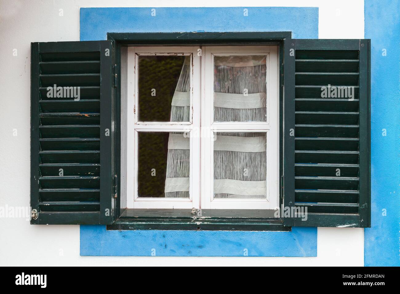 Fenêtre avec volets vert foncé ouverts dans un cadre bleu. Architecture rurale du village de Santana, île de Madère, Portugal Banque D'Images