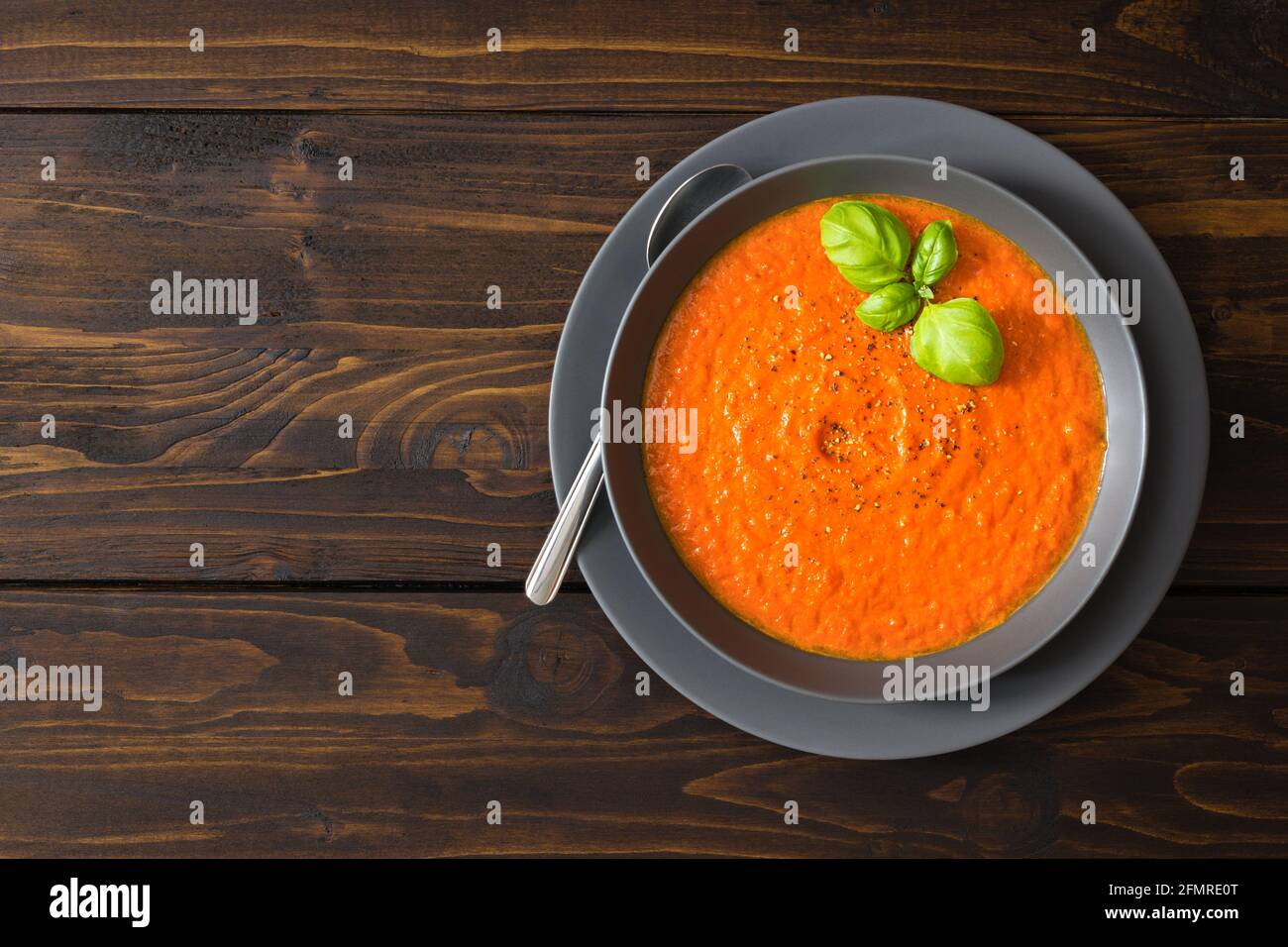 Une assiette remplie de soupe de tomates maison garnie de frais basilic sur fond de bois Banque D'Images