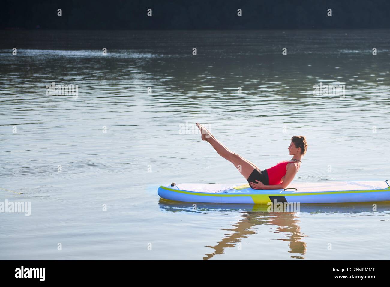 Femme méditant et pratiquant le yoga au lever du soleil en paddle board Banque D'Images