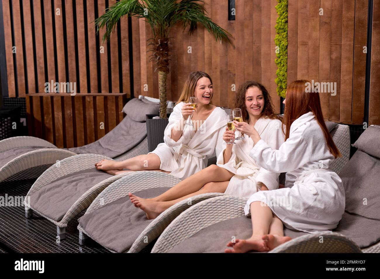 Les femmes sympathiques aiment boire du champagne au spa. Trois belles femmes caucasiennes portant des peignoirs ayant un repos frais, vacances dans le centre de bien-être Banque D'Images