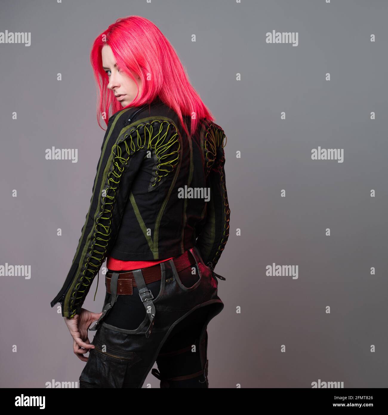 Style kitsch, mode du futur. Mélange de styles. Une jeune femme avec des cheveux écarlate lumineux dans des vêtements sombres inhabituels sur fond gris. Banque D'Images