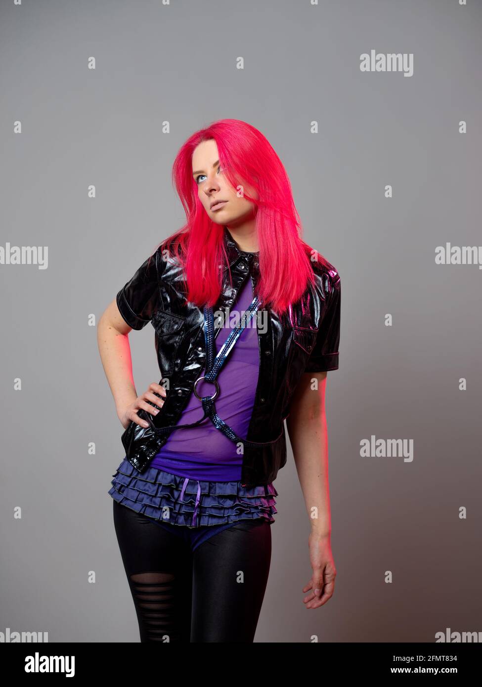 Style kitsch, mode du futur. Mélange de styles. Une jeune femme avec des cheveux écarlate lumineux dans des vêtements sombres inhabituels sur fond gris. Banque D'Images
