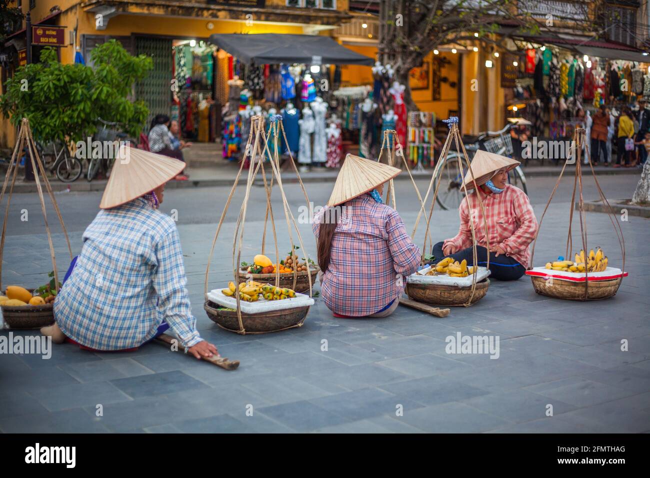 Les hustlers vietnamiens portant des paniers jumeaux et des bâtons d'épaule attendent que les touristes prêtent leurs marchandises pour des occasions photographiques, Hoi an, Vietnam Banque D'Images