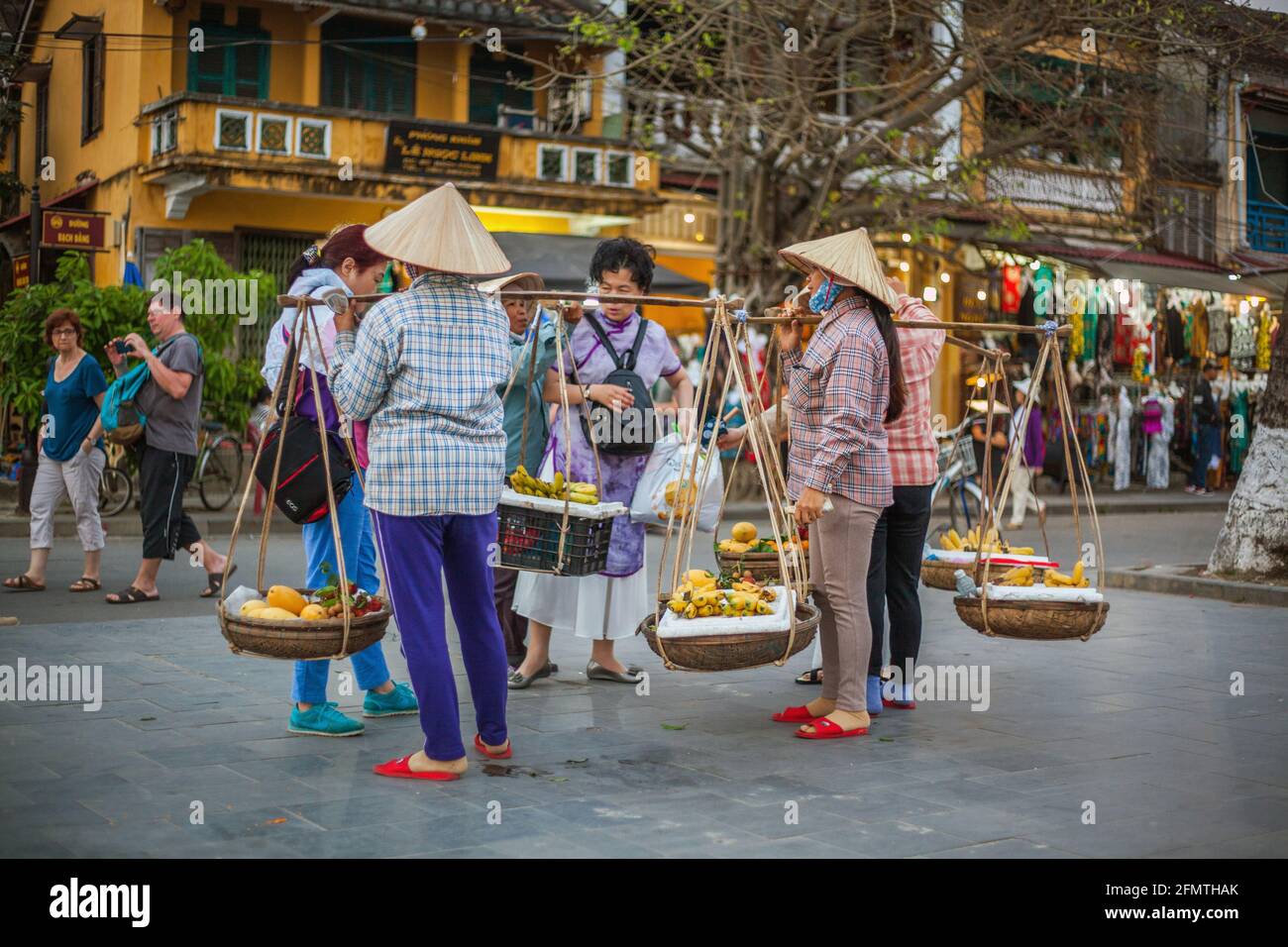 Les amateurs de fruits vietnamiens portant des paniers jumeaux et des bâtons d'épaule offrant aux touristes leurs marchandises pour des occasions photographiques, Hoi an, Vietnam Banque D'Images