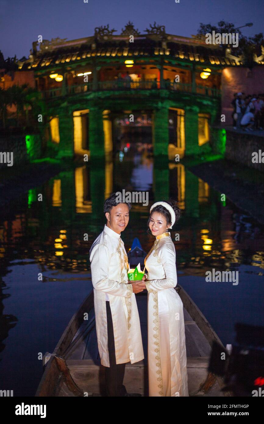 Couple vietnamien debout en bateau devant le pont japonais libérer des lanternes flottantes colorées dans la rivière, Hoi an, Vietnam Banque D'Images