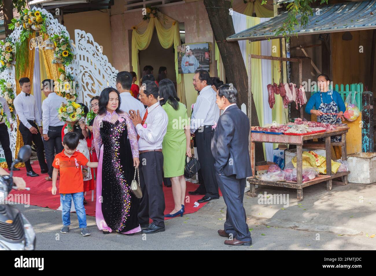Les invités de mariage attendent à l'extérieur du hall de réception à côté de la stalle de marché vendant de la viande, Hoi an, Vietnam Banque D'Images
