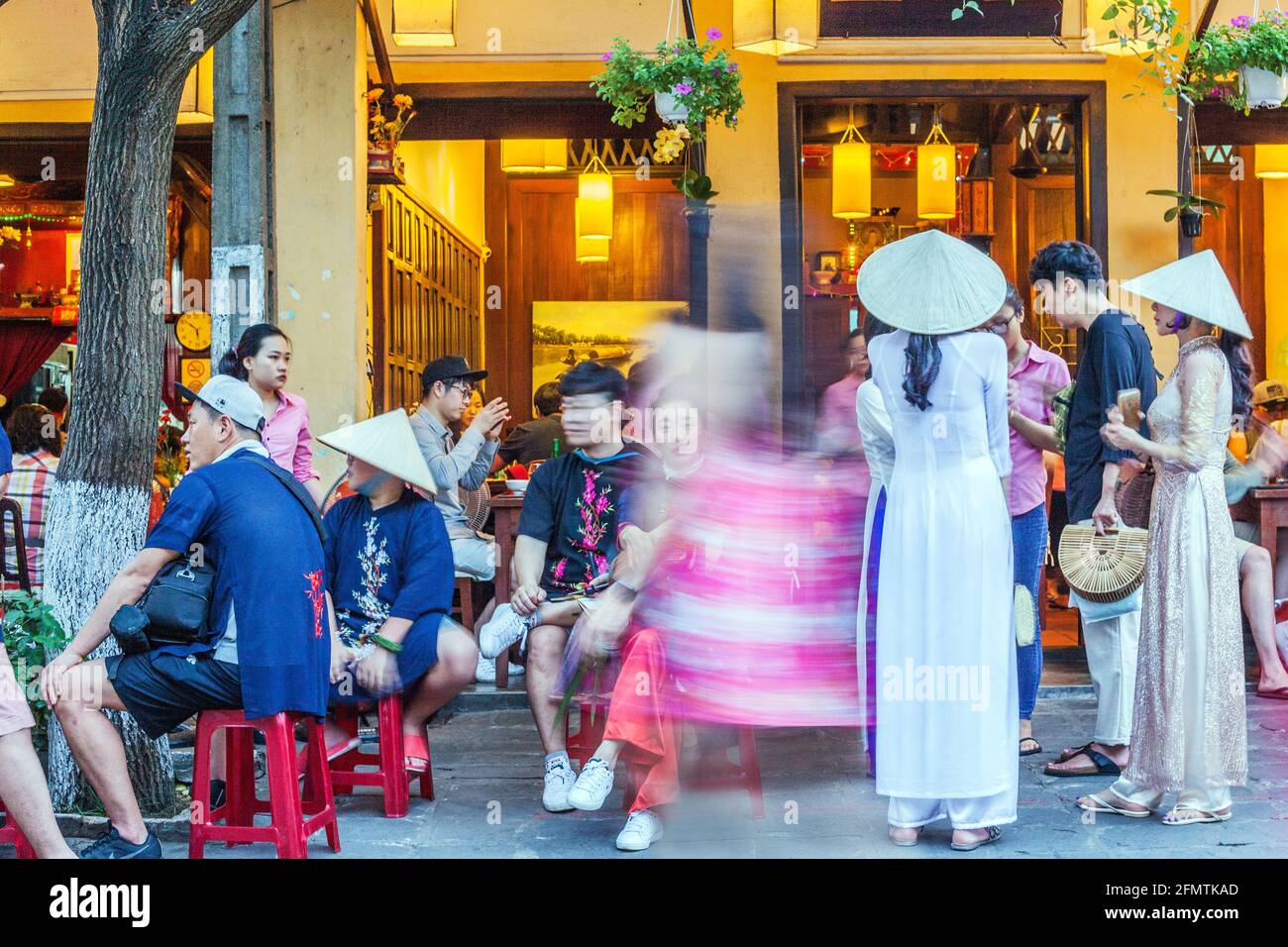 De jolies femmes vietnamiennes portant des chapeaux coniques et des robes traditionnelles d'ao dai se tiennent à l'extérieur du restaurant dans la vieille ville, Hoi an, Vietnam Banque D'Images