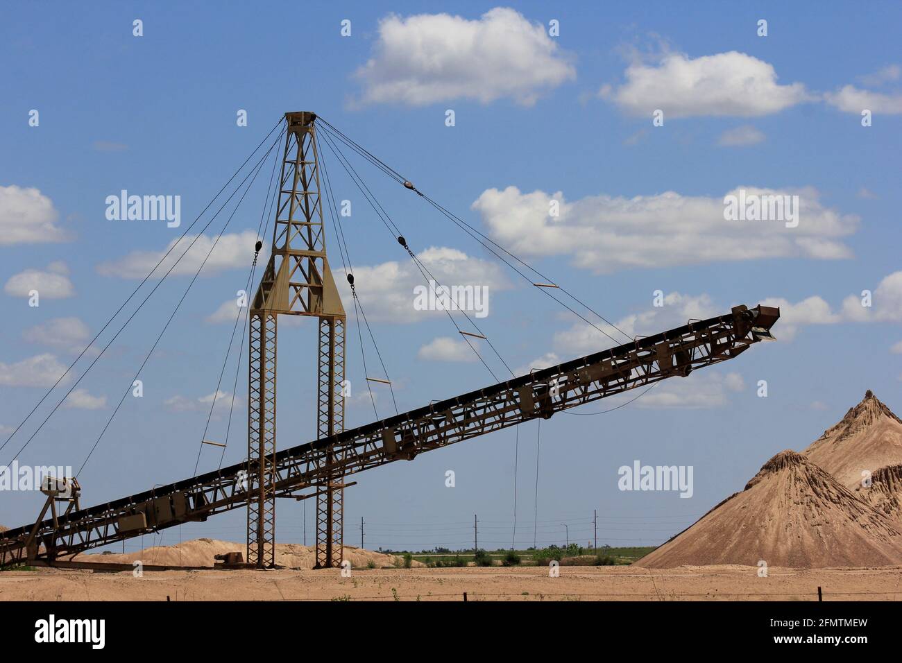 Un sable avec un tapis roulant qui déplace le sable jusqu'à la pile avec le ciel bleu et les nuages blancs qui est lumineux et coloré au Kansas. Banque D'Images