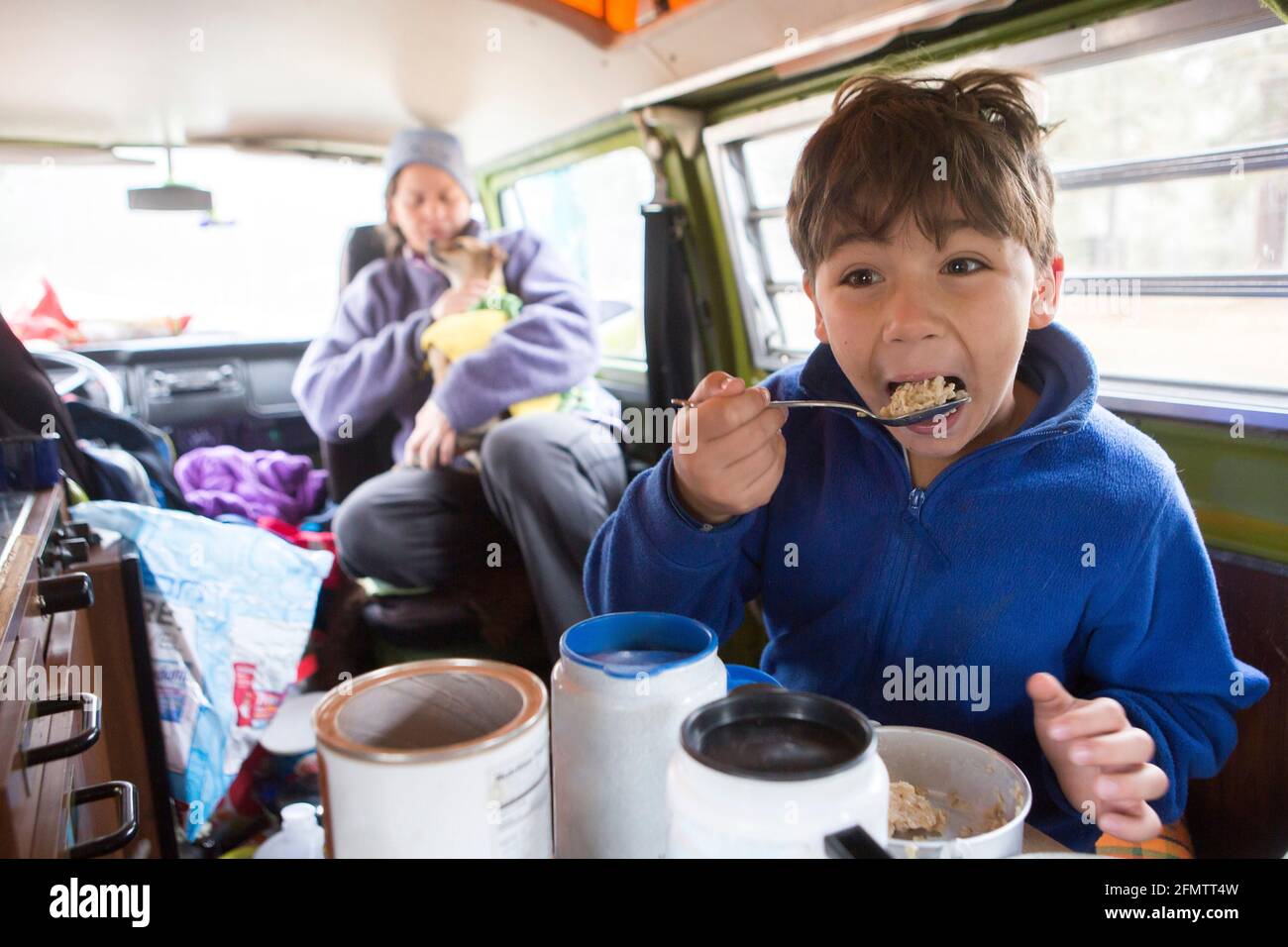 Un garçon de 8 ans mange des flocons d'avoine dans la fourgonnette VW Camper lors d'un voyage en famille Banque D'Images