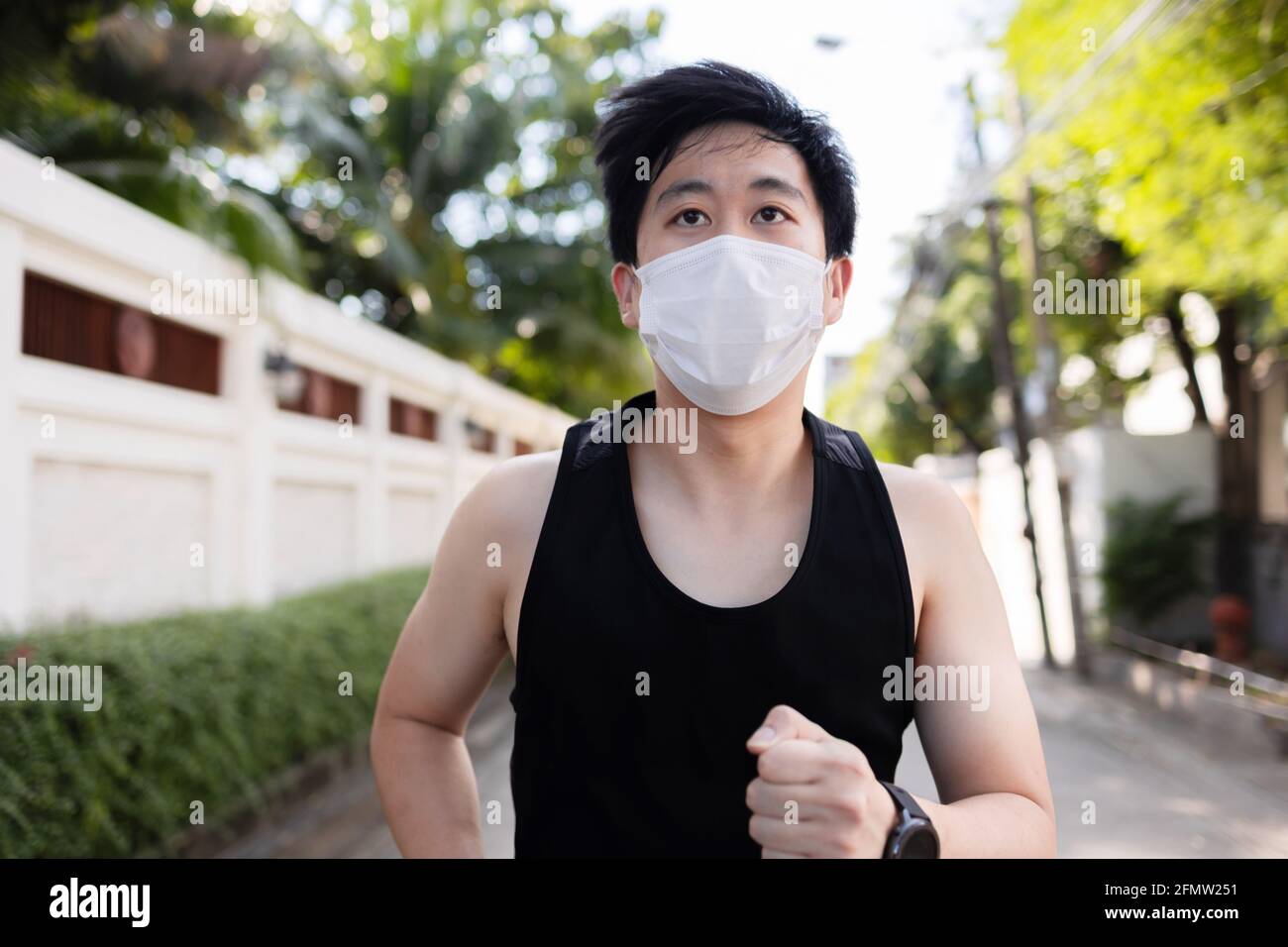 Jeune asiatique courant avec un masque facial dans la ville. Un coureur de sexe masculin fait de l'exercice et du jogging dans la rue Banque D'Images