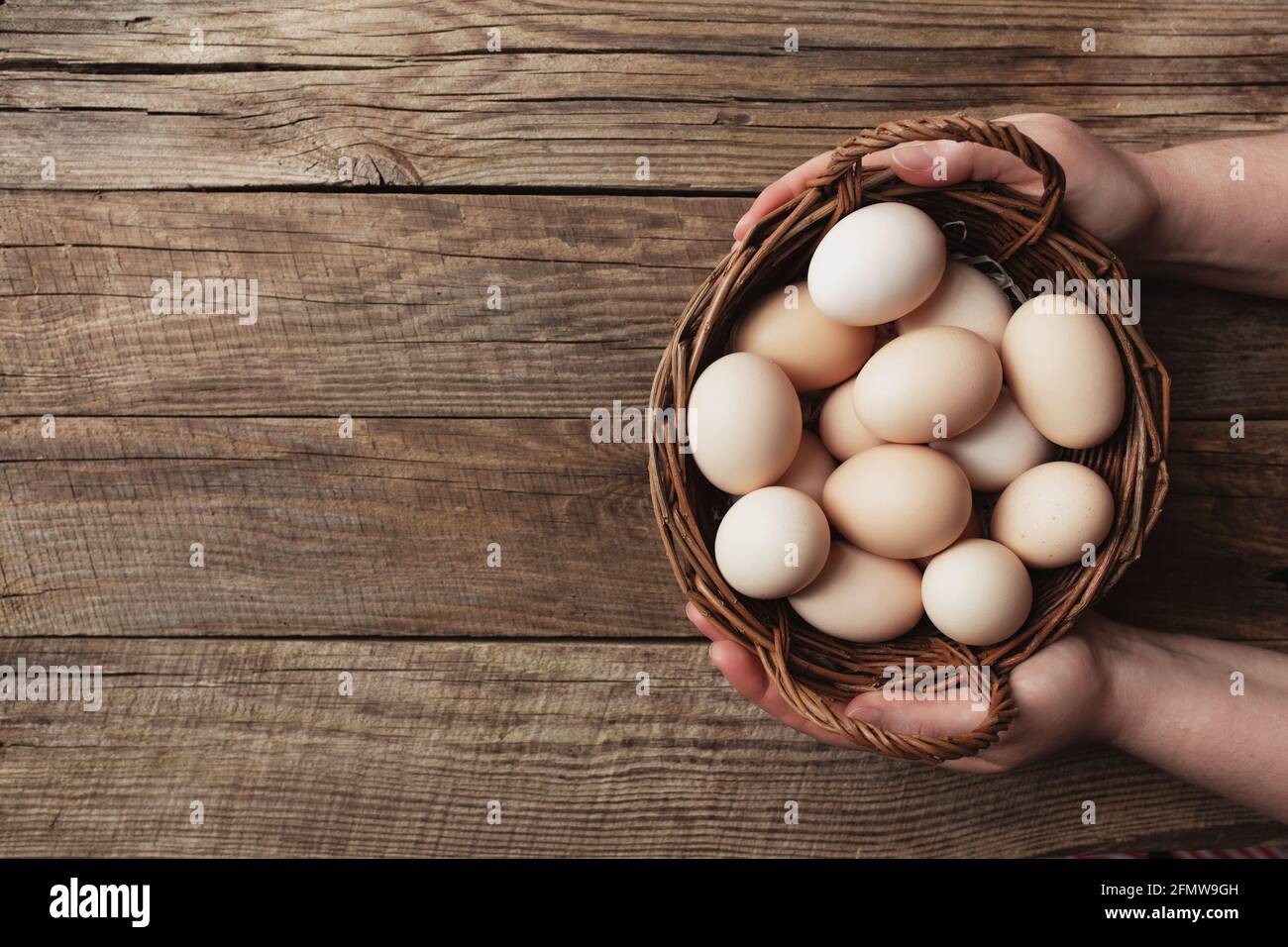 Pondre à plat avec les mains tenant le panier avec des œufs de poulet bio sur fond de bois. Concept de ménage biologique avec des oeufs de la gamme libre et de pâturage rai Banque D'Images