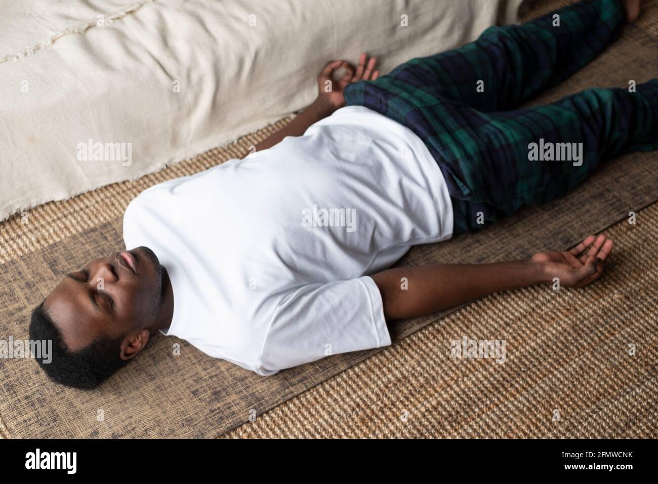 Jeune homme noir allongé dans l'exercice de corps mort ou la pose de cadavre avec ses yeux fermés, pose de Savasana Banque D'Images