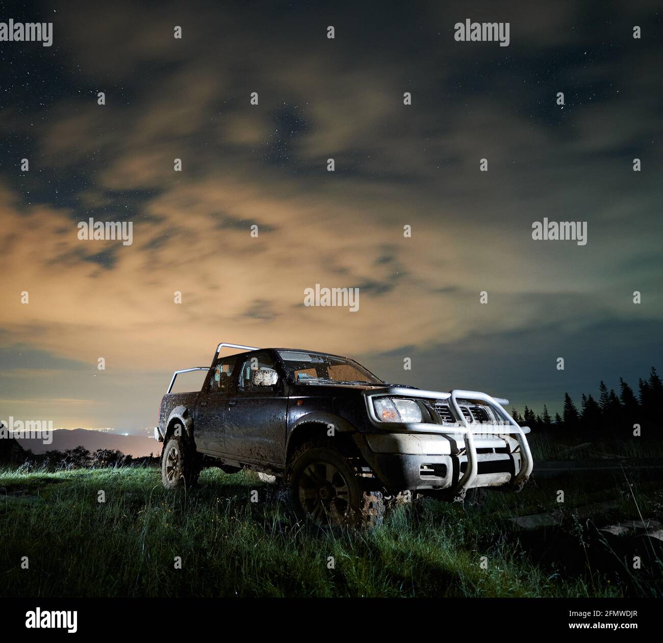 Camionnette éclairée en camion dans la boue sur la prairie montagneuse la nuit sous ciel étoilé nuageux. Espace de copie, vue de face. Concept de conduite extrême Banque D'Images