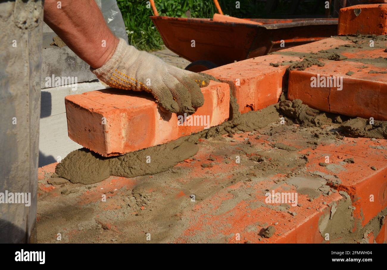 Une personne maçon pose un mur de briques ou la fondation d'une nouvelle maison. Un gros plan d'un brickwork quand un constructeur pose un cours de briques sur le mortier. Banque D'Images