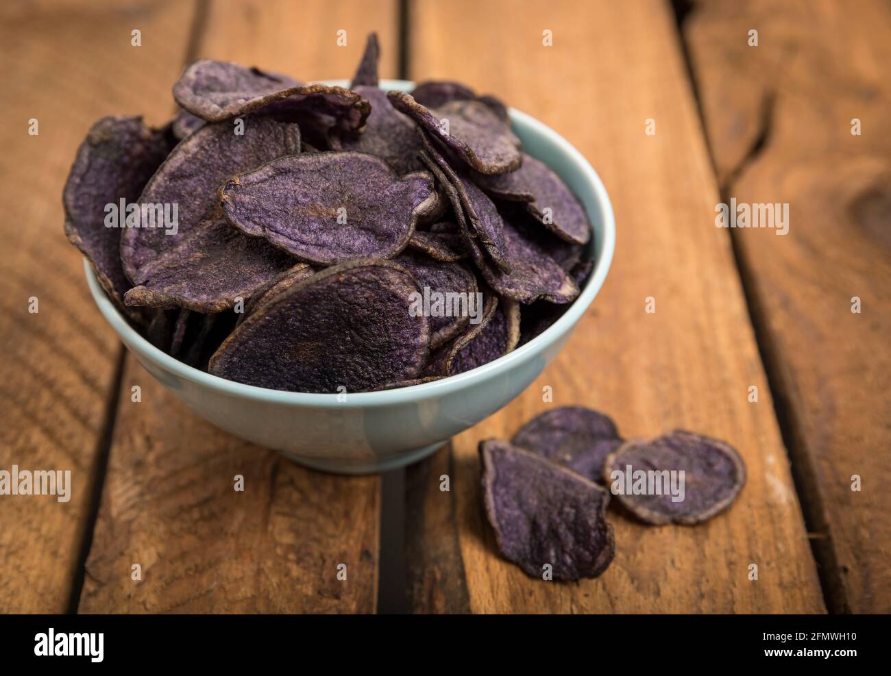 Chips de pommes de terre à base de pommes de terre violettes dans un bol turquoise sur une table en bois rustique Banque D'Images