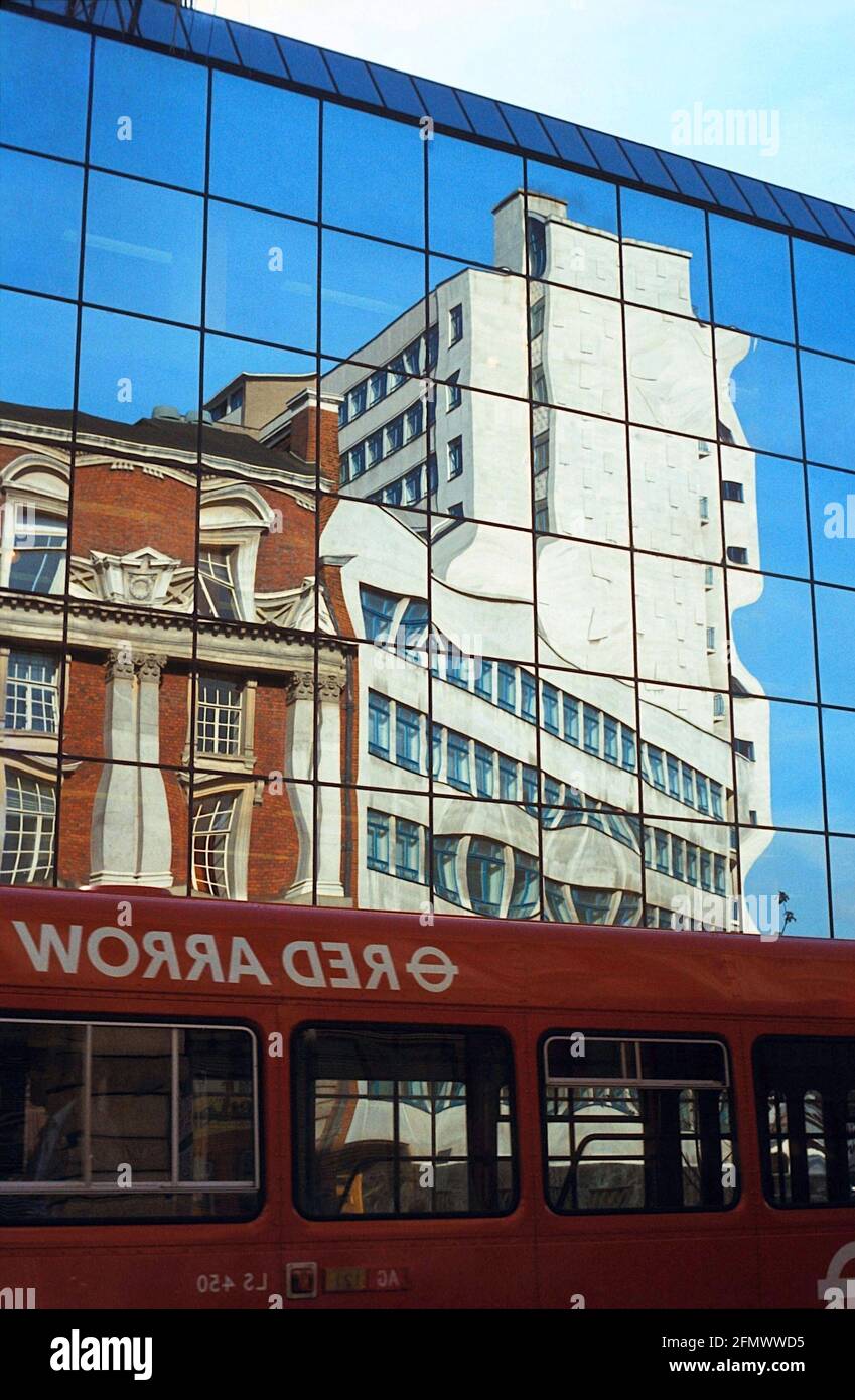 Réflexions sur un bâtiment à façade de verre avec un bus rouge au premier plan. Photo vintage de 1985 Banque D'Images