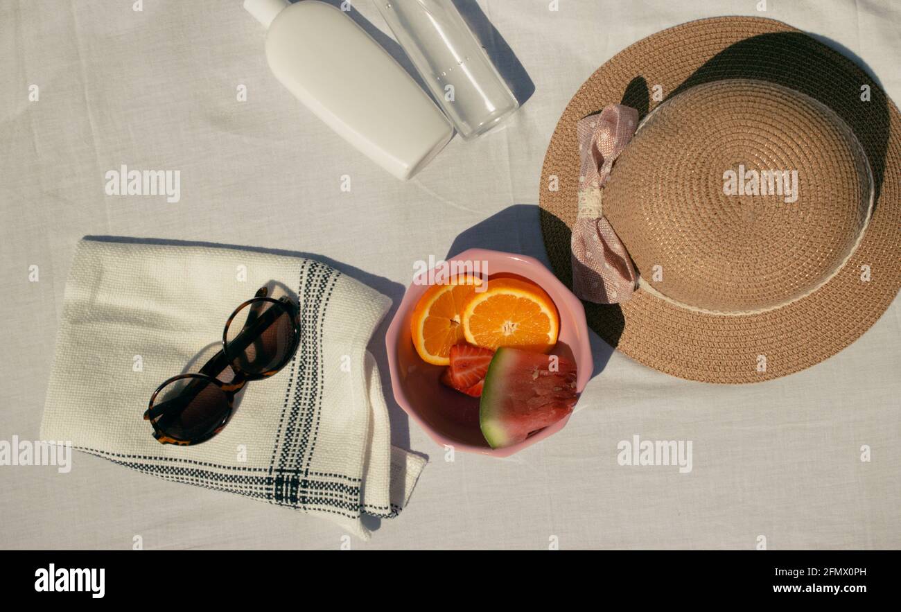 Image horizontale de fruits (orange, pastèque, fraises) dans un bol rose avec des objets d'été sur fond de tissu blanc. Été 2021 Banque D'Images