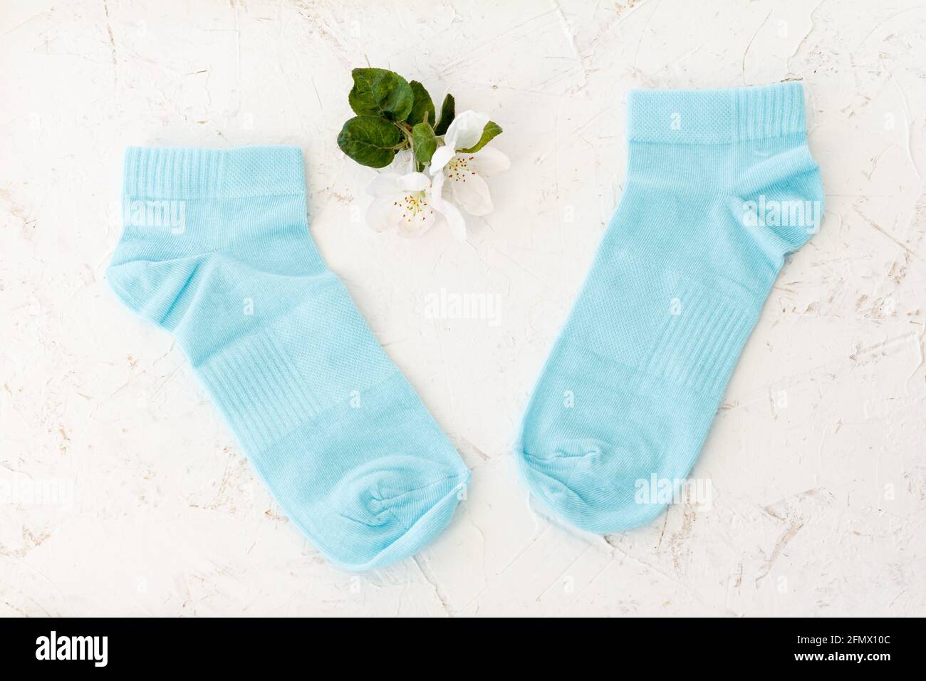 Paire de chaussettes bleues pour femmes et fleurs d'un pommier sur fond blanc structuré, vue du dessus. Banque D'Images