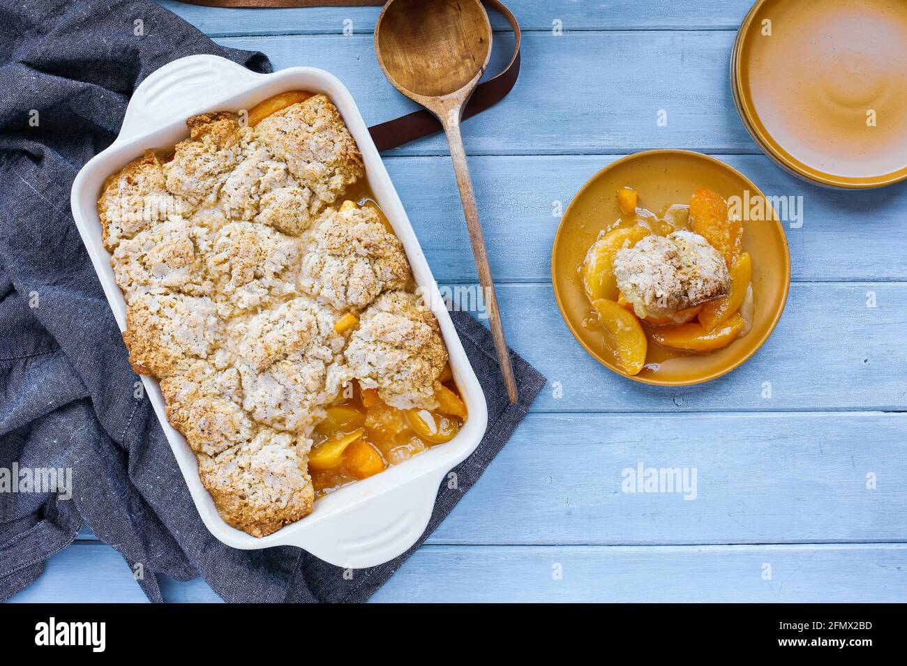 Portion de biscuit fraîchement cuit, cobbler à la pêche avec tablier et cuillère en bois prise depuis la vue de dessus. Banque D'Images