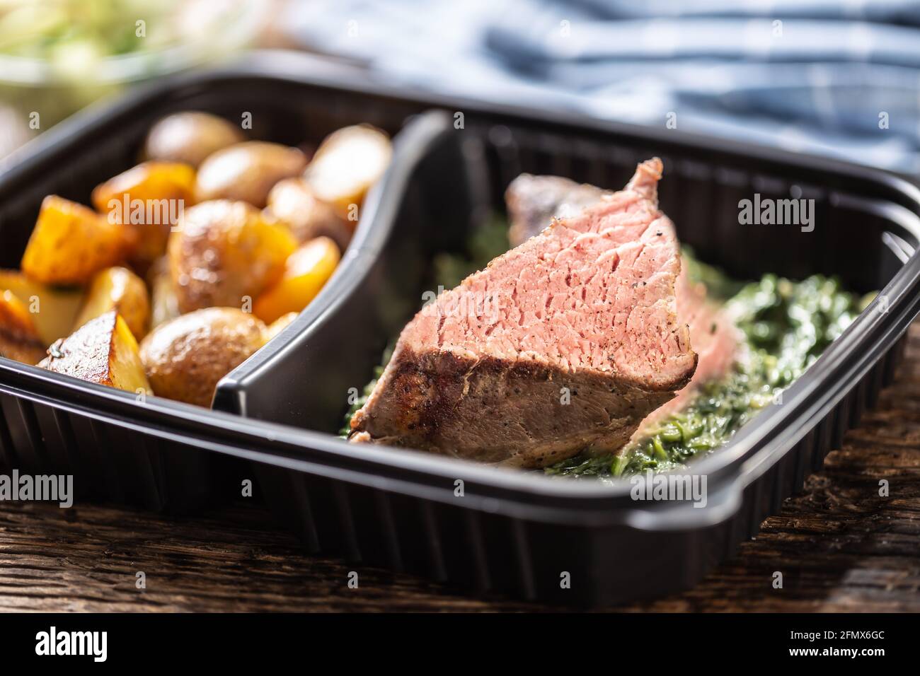 Délicieux steak de viande rouge sous vide emballé dans un plat à emporter boîte en plastique et servie avec des pommes de terre croquantes rôties et sauce aux épinards et frais Banque D'Images