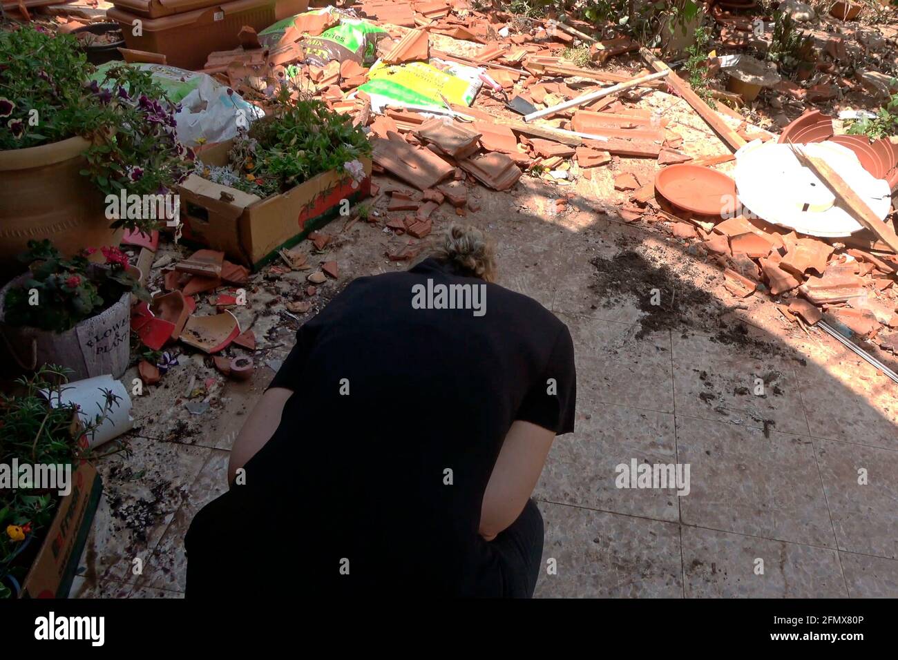 Une israélienne prend la couverture sur le sol alors que des sirènes d'attaque aérienne partent dans la cour d'une maison qui a été frappée par une roquette lancée depuis la bande de Gaza le 11 mai 2021 à Ashkelon, en Israël. De lourds échanges de feu se poursuivent entre les militants palestiniens et l'armée israélienne. Les militants ont tiré plus de 300 roquettes vers Israël depuis lundi soir, tandis qu'Israël a touché plus de 150 cibles à Gaza en réponse. Banque D'Images