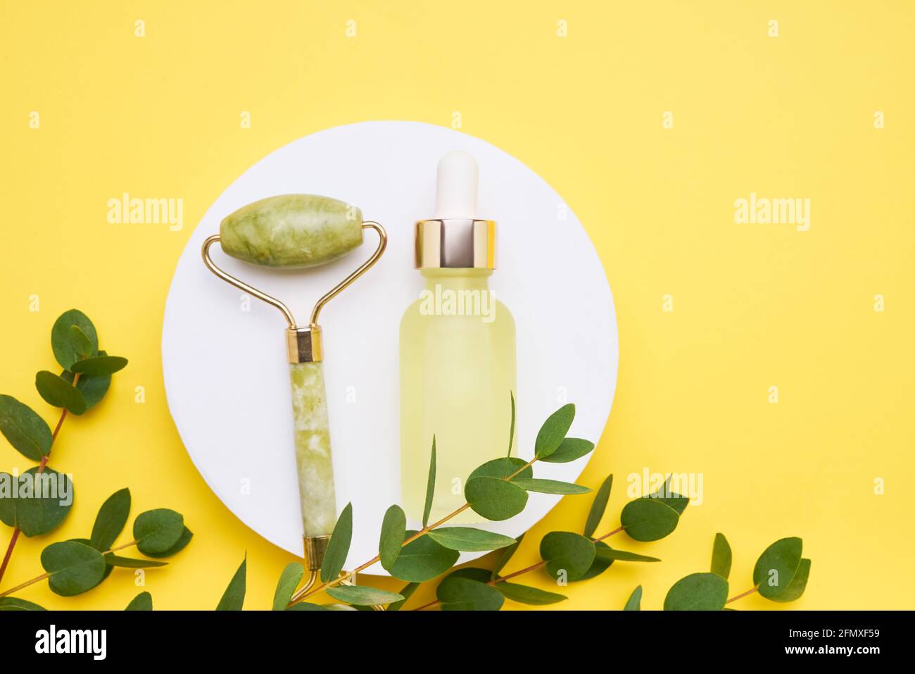 Flacon compte-gouttes en verre jaune à usage médical et cosmétique, rouleau de jade et branche d'eucalyptus sur fond jaune vif. Concept SPA. Vue de dessus, copie Banque D'Images