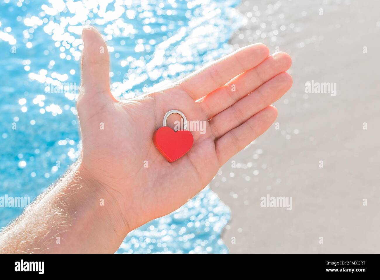 Dans La Main D Un Homme Sur La Paume D Un Petit Coeur Rouge Gros Plan Sous La Forme D Une Serrure Un Signe Ou Un Symbole D Amour Contre La Cote De Mer Photo Stock