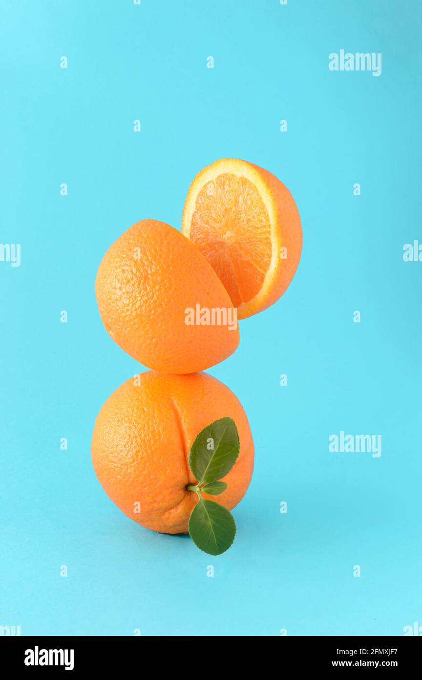 Orange entier avec une feuille verte et sur elle une coupe orange en deux sur un fond bleu. Concept d'été agrumes, jus de fruits rafraîchissants. Couleurs vibrantes. Banque D'Images