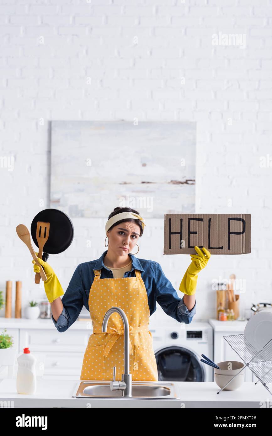 Triste femme de ménage tenant l'étiquette avec aide lettrage et ustensile  dedans cuisine Photo Stock - Alamy