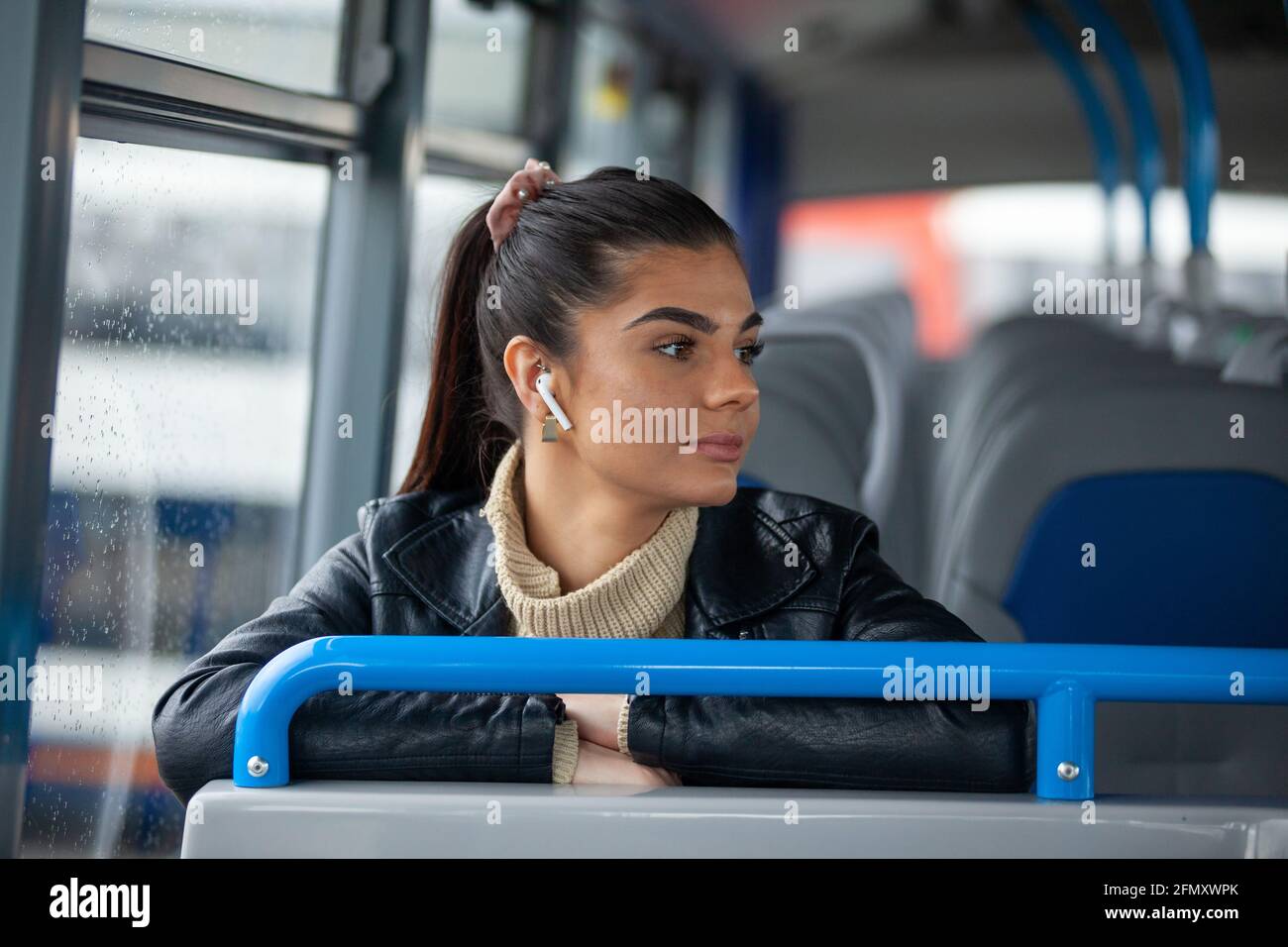 Une belle femme assise dans un bus et à l'écoute de la musique à travers ses écouteurs Banque D'Images