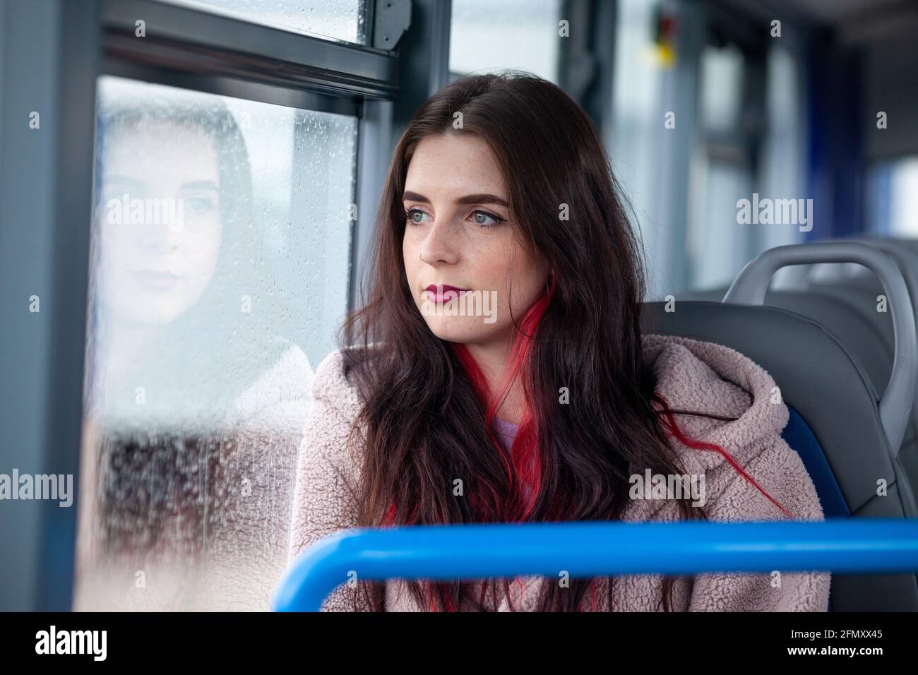 Une femme voyageant dans un bus et regardant à l'extérieur une fenêtre imbibée de pluie Banque D'Images