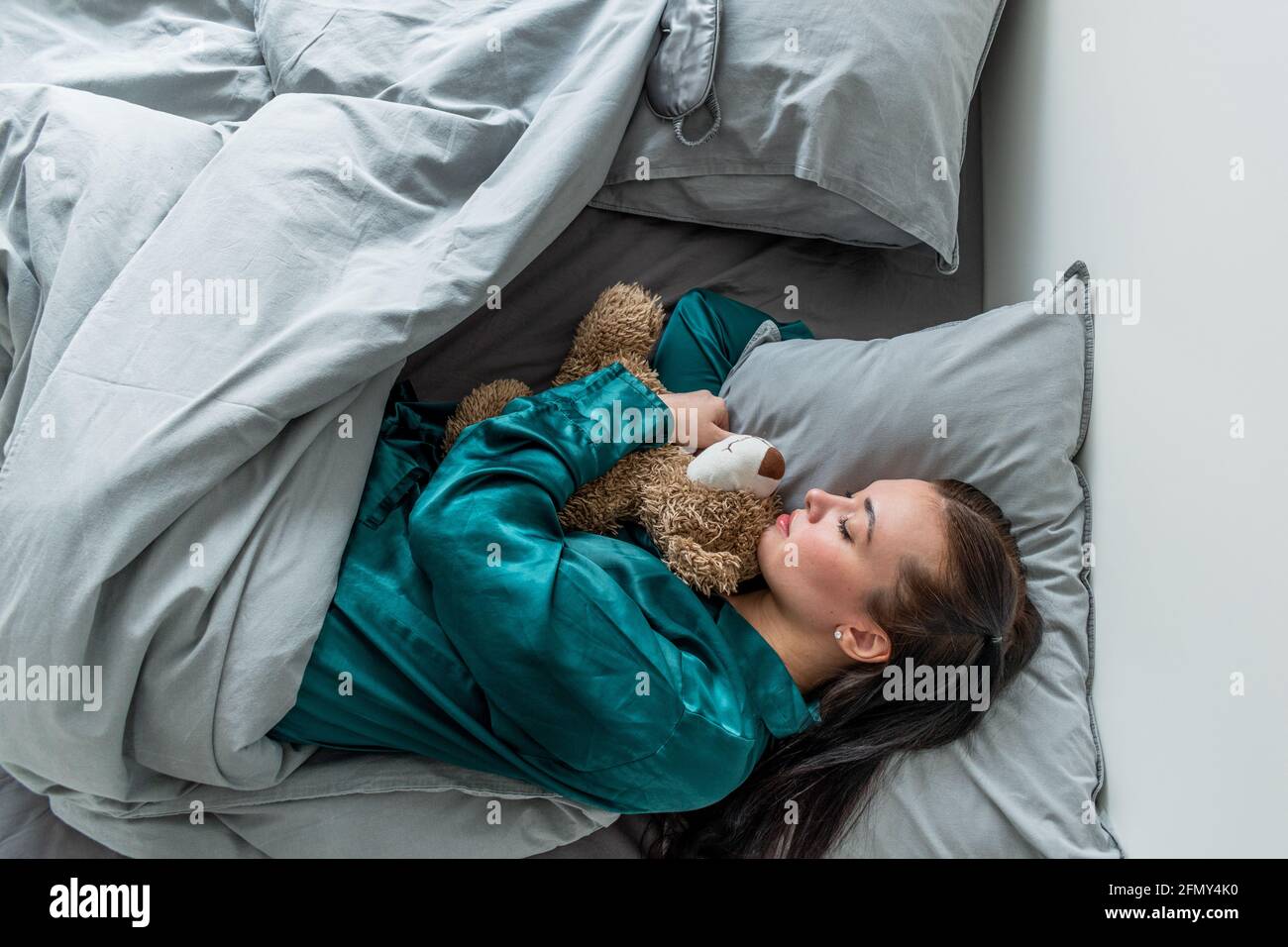 Une jeune femme en pyjama de soie dorment sur le lit et épouse un ours en peluche. Retour aux racines. Concept bien-être. Banque D'Images