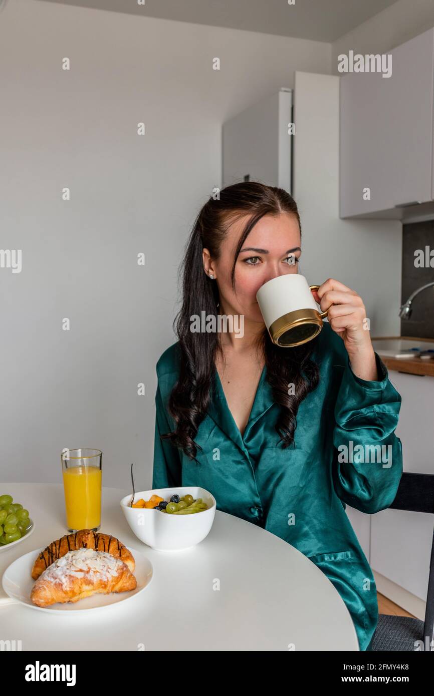 Jeune femme pyjama en soie a le petit déjeuner et boissons café dans la cuisine à la maison. Concept bien-être. Banque D'Images