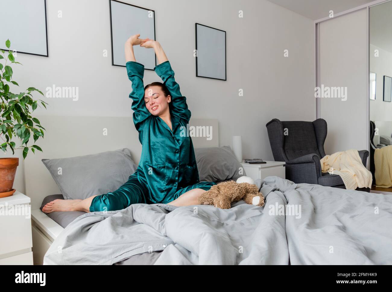 Jeune femme dans des yawns de pyjama en soie tout en étant assise dans un confortable lit doux. Banque D'Images