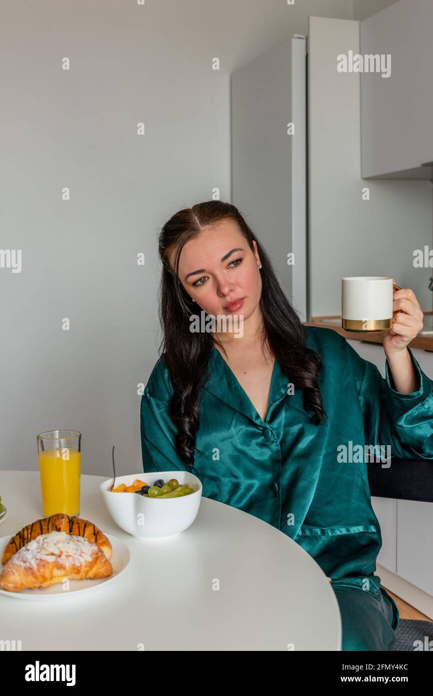 Jeune femme pyjama en soie a le petit déjeuner et boissons café dans la cuisine à la maison. Concept bien-être. Banque D'Images