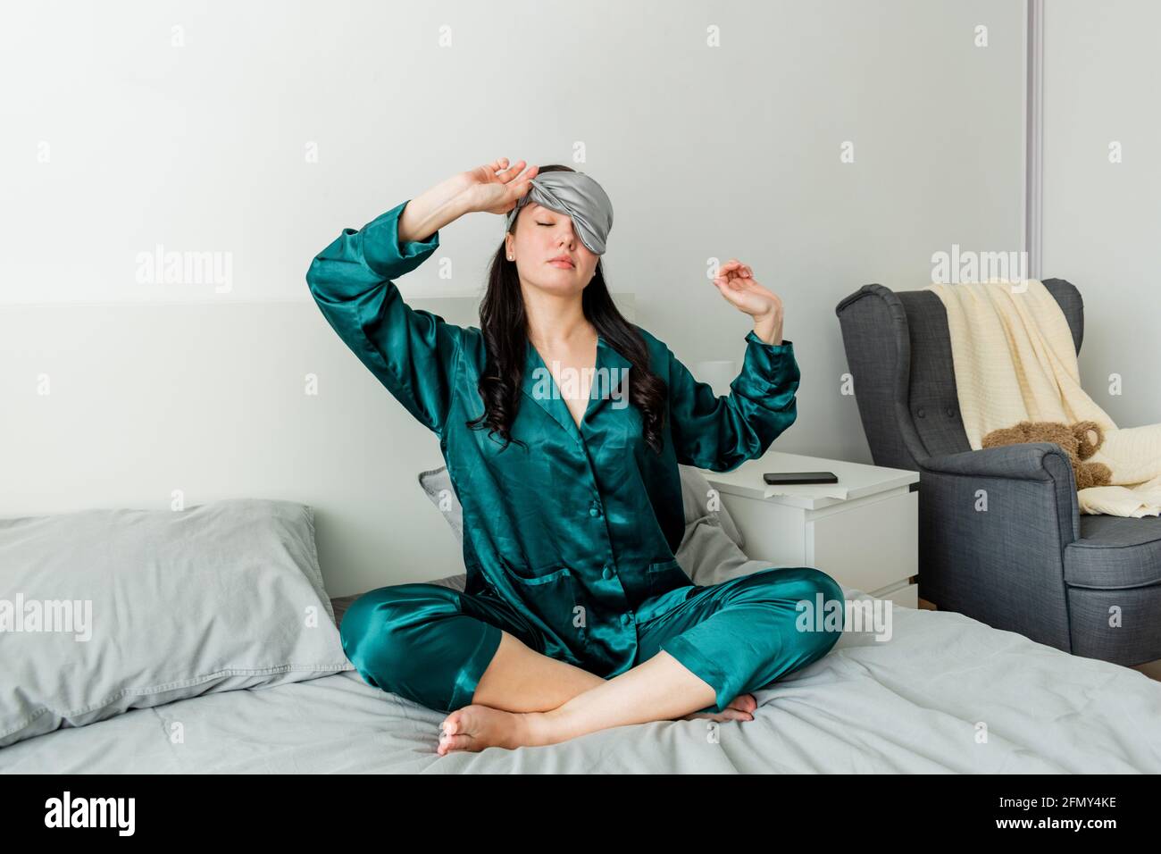 Jeune femme dans des yawns de pyjama en soie tout en étant assise dans un confortable lit doux. Banque D'Images