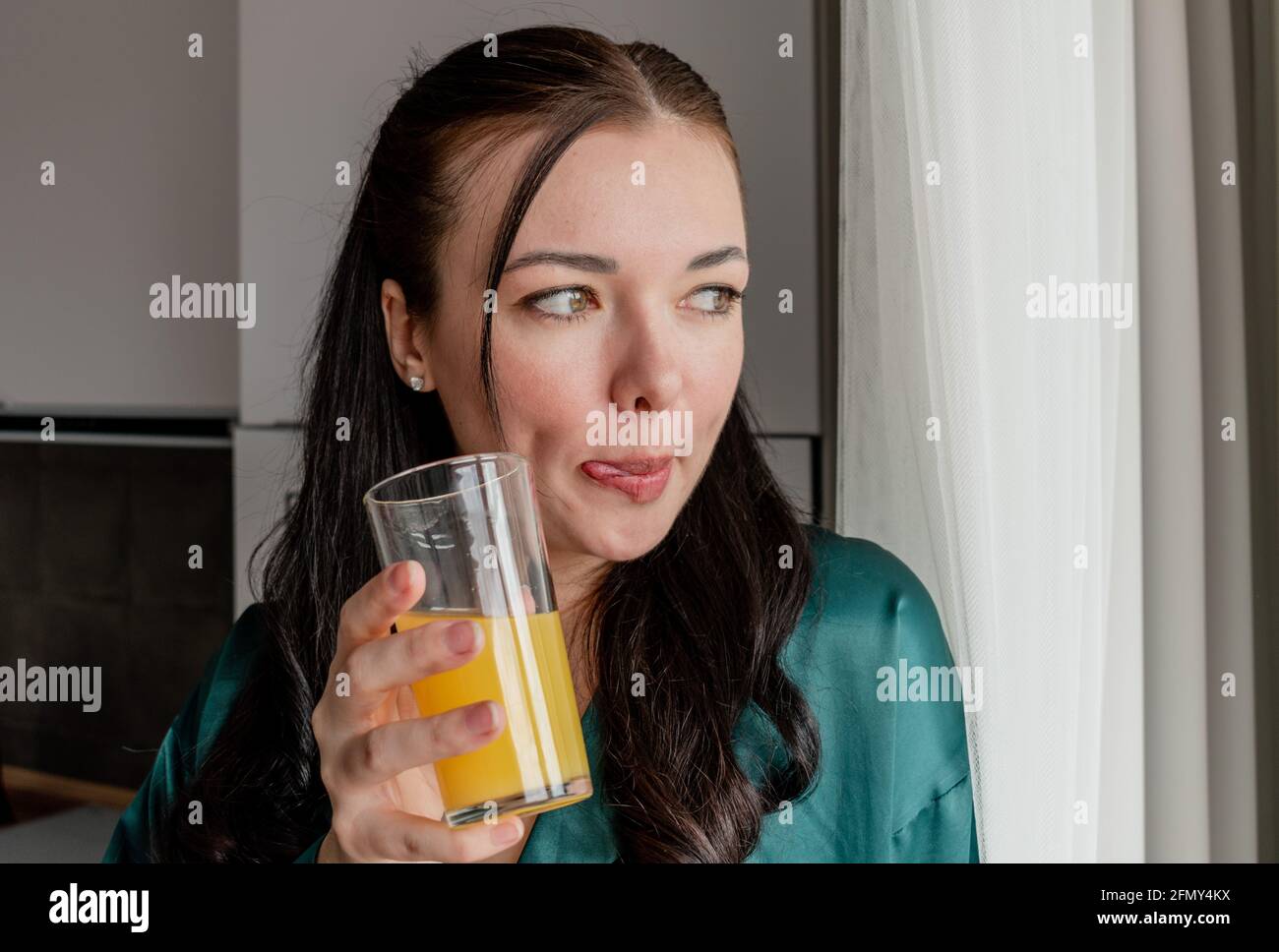 La jeune femme boit du jus de la tasse debout près de la fenêtre. Concept de bien-être et zone de confort à la maison. Banque D'Images