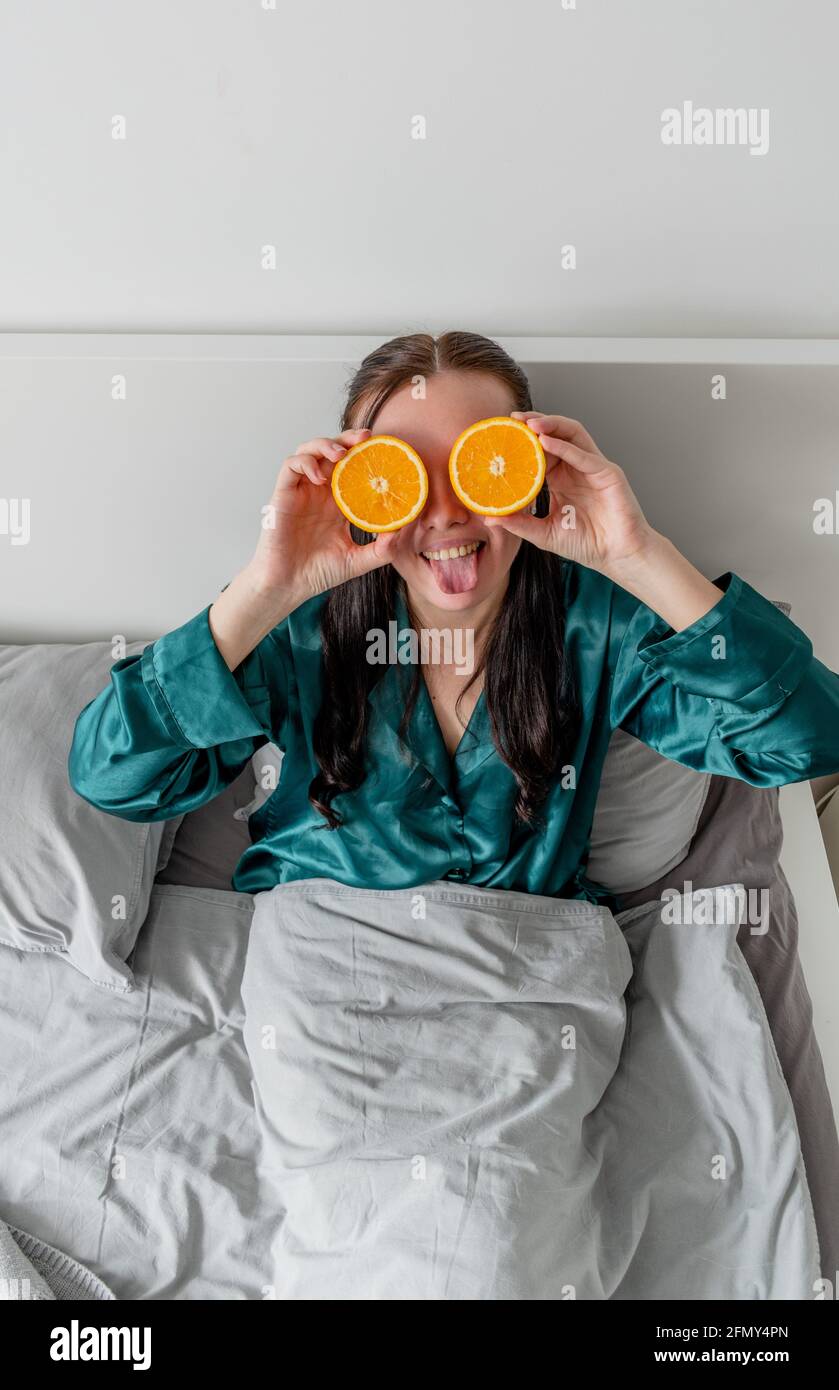 La jeune femme rit et tient les oranges près de ses yeux. Concept de bien-être et zone de confort à la maison. Banque D'Images