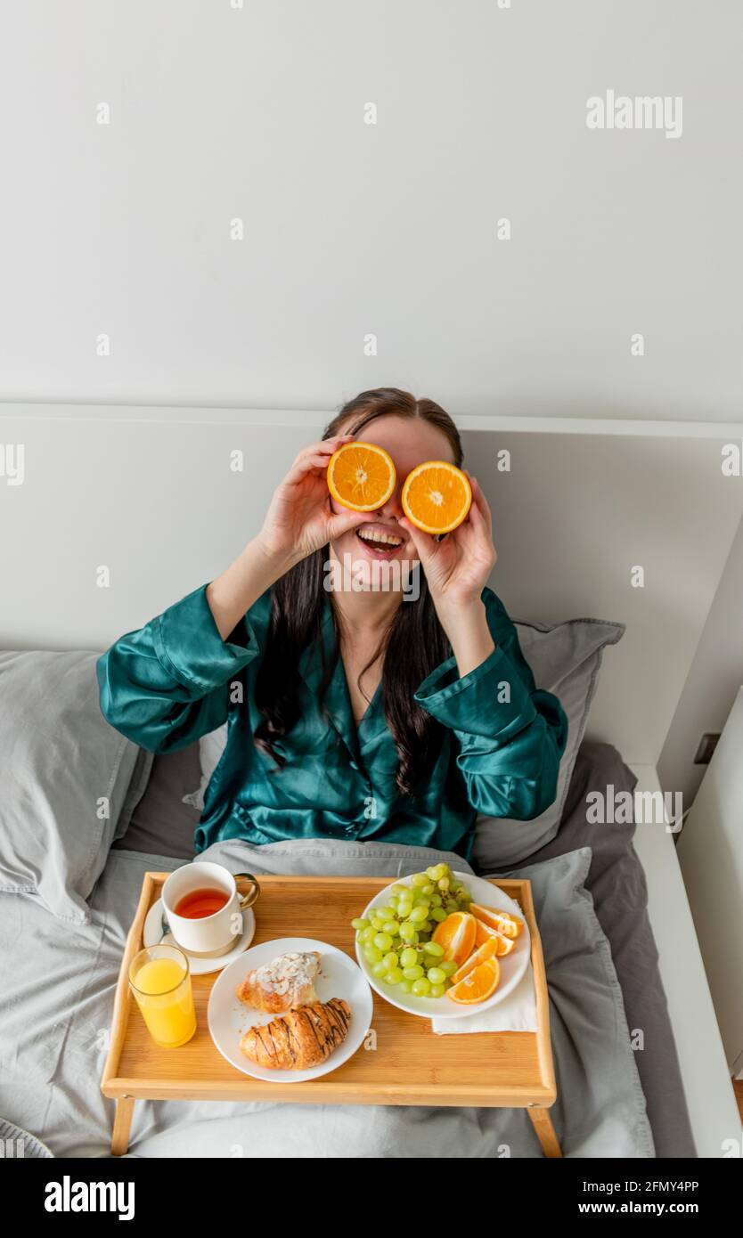 La jeune femme rit et tient les oranges près de ses yeux. Concept de bien-être et zone de confort à la maison. Banque D'Images